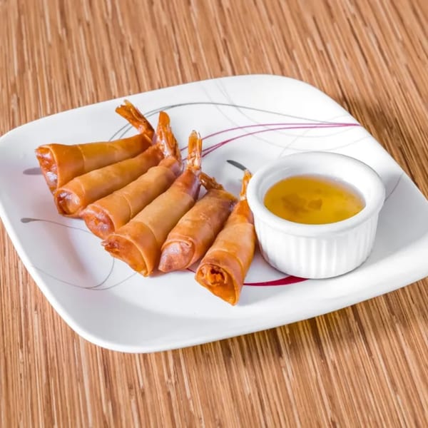 Golden fried shrimp rolls with tails visible, served with a side of sweet chili sauce.