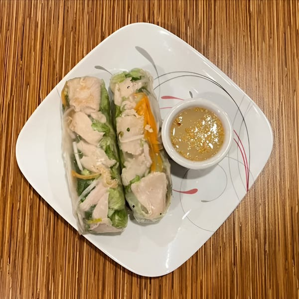 Two fresh spring rolls with chicken and vegetables, served with a dipping sauce on a white plate.
