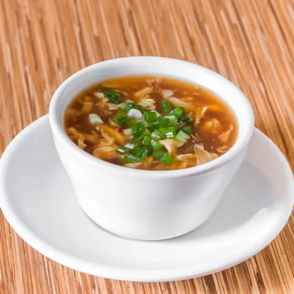 Hot and sour soup with green onions in a white cup on a wooden table.