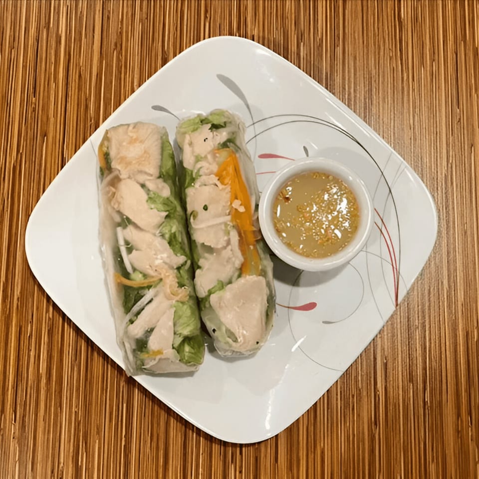 Two fresh spring rolls filled with chicken and vegetables, served with a peanut dipping sauce.