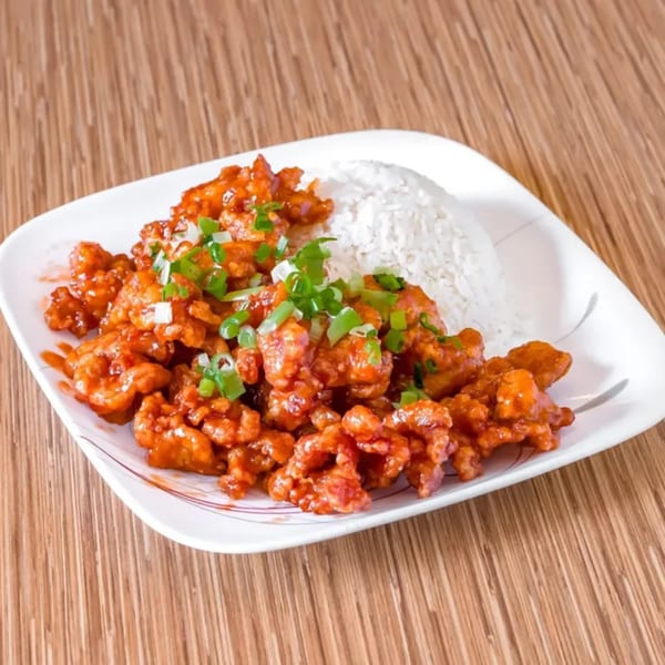 A white plate of Bangkok Cuisine's orange chicken with white rice, garnished with green onions.
