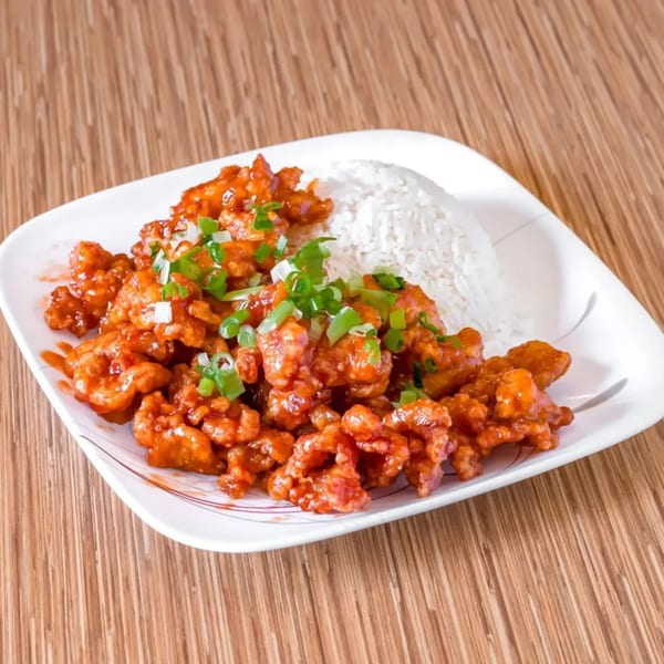 Sweet and sour chicken with white rice and green onions on a white plate.