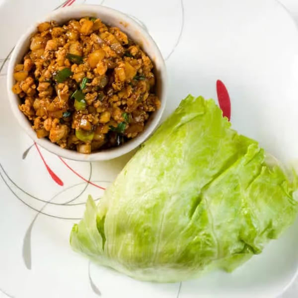 Thai lettuce wraps with a bowl of minced chicken and a fresh lettuce leaf on a white plate.