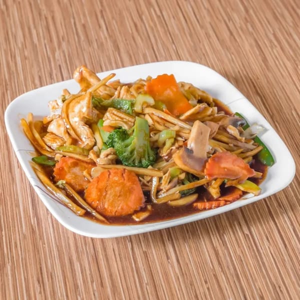A white square plate filled with Bangkok Cuisine's stir-fried chicken, broccoli, carrots, and mushrooms in a rich sauce.