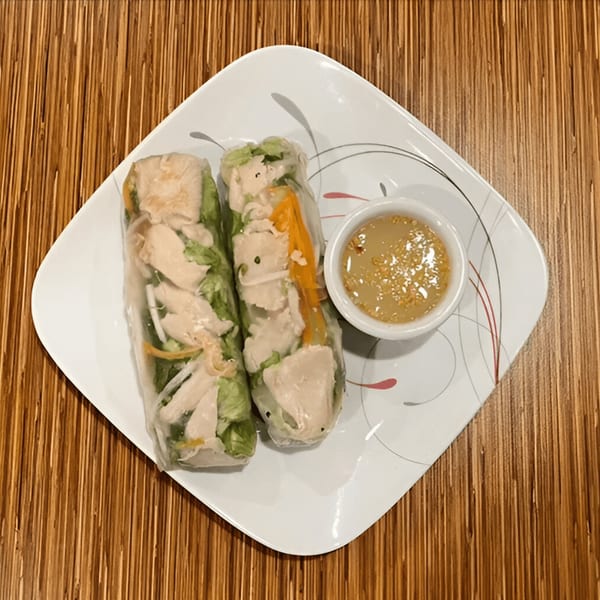 Two fresh spring rolls filled with chicken and vegetables, served with a peanut dipping sauce.
